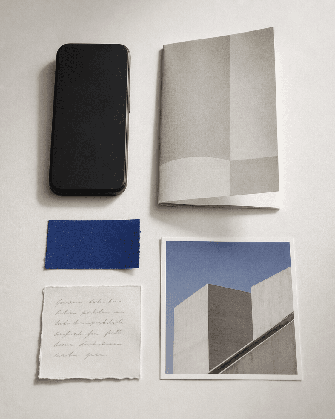 A phone, architecture print, folded leaflet, cobalt swatch, and handwritten note arranged on a desk